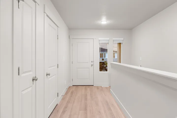Wood-finish flooring leading to a paneled entry door with sidelight window, accompanied by two paneled doors and a white painted half-wall