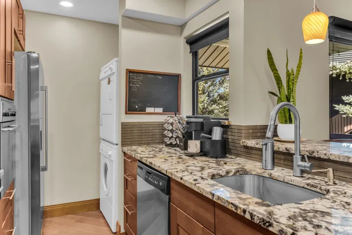 Stainless steel appliances, built-in stacked laundry units, wood-finish cabinetry, stone countertops, and an undermount sink
