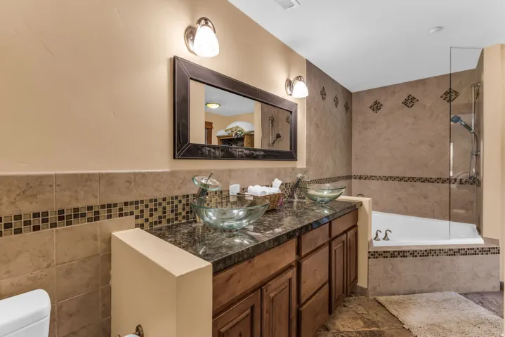 Bathroom featuring a dual vanity with vessel sinks, stone countertops, wood-finish cabinetry, and a combination shower-tub with tile surround