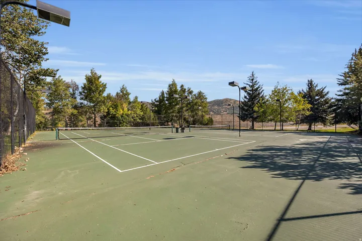 Tennis court with perimeter fencing, net, and multiple overhead lights