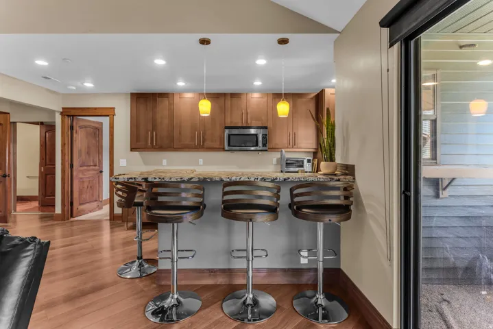 Kitchenette with wood-finish cabinetry, stone countertop, stainless steel microwave, and recessed lighting