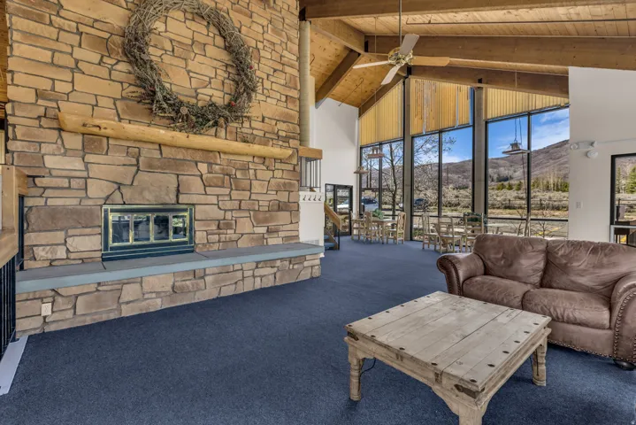 Stone fireplace with a hearth, vaulted wood-beam ceilings, expansive floor-to-ceiling windows, and wall-mounted lighting