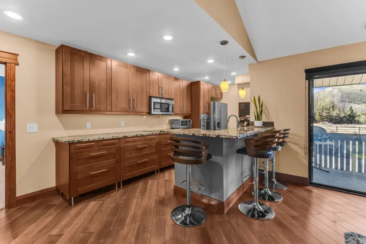 Wood-finish flooring with an expansive kitchen featuring wood cabinetry, granite countertops, recessed lighting, and a built-in microwave