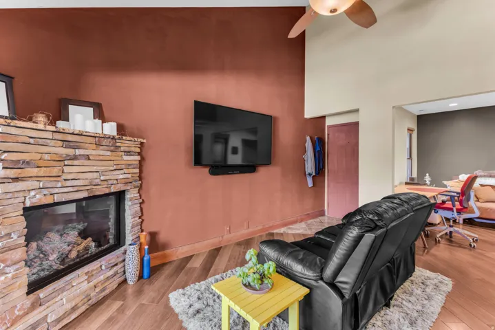 Stacked stone fireplace with a glass-fronted firebox, wood-finish flooring, and a ceiling fan