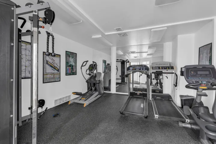 Dedicated fitness area with rubberized flooring, mirrored wall, and recessed ceiling lights