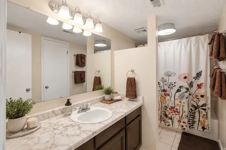 Vanity with a single basin sink and a marble-finish countertop, dark wood-finish cabinetry, chrome fixtures, and a multi-bulb vanity light