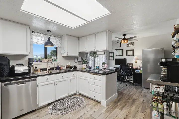 White cabinetry, dark stone-finish countertops, stainless steel appliances, wood-finish flooring, and an upgraded ceiling-mounted light panel.