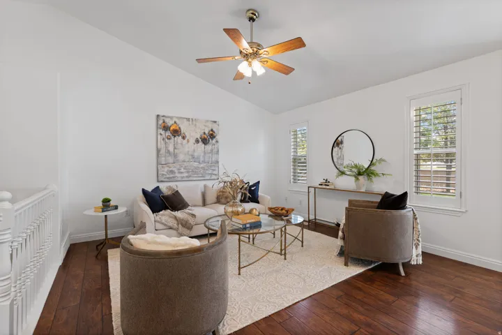 Hardwood-finish flooring, vaulted ceiling with a ceiling fan, white window shutters, and white wall finishes