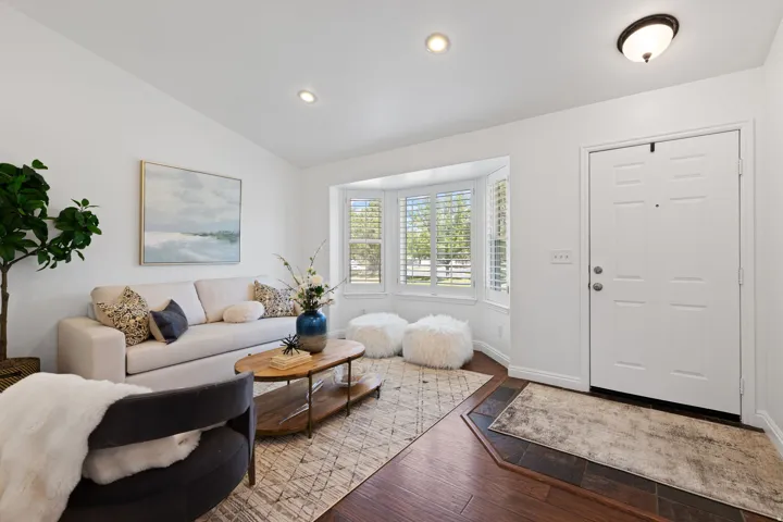 Bay window with plantation shutters, recessed lighting, white paneled entry door, wood-finish flooring, and tile flooring