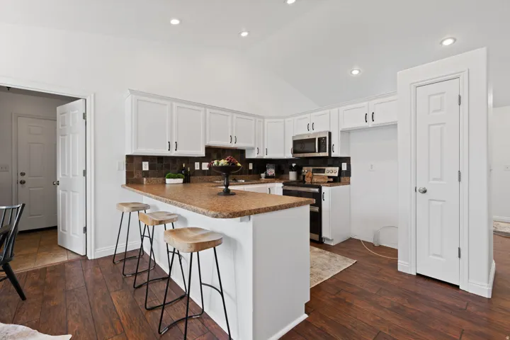 Kitchen featuring white cabinetry, stainless steel microwave, wood-finish flooring, and a breakfast bar with stone-finish countertop