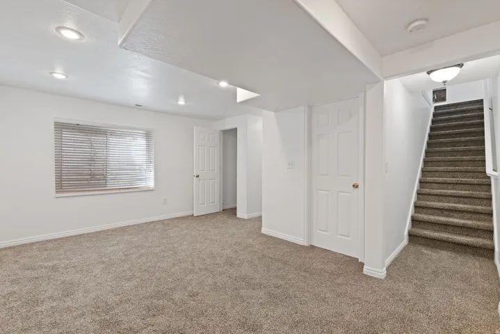 Recessed ceiling lighting, multiple doorways, a window with blinds, and carpeted flooring
