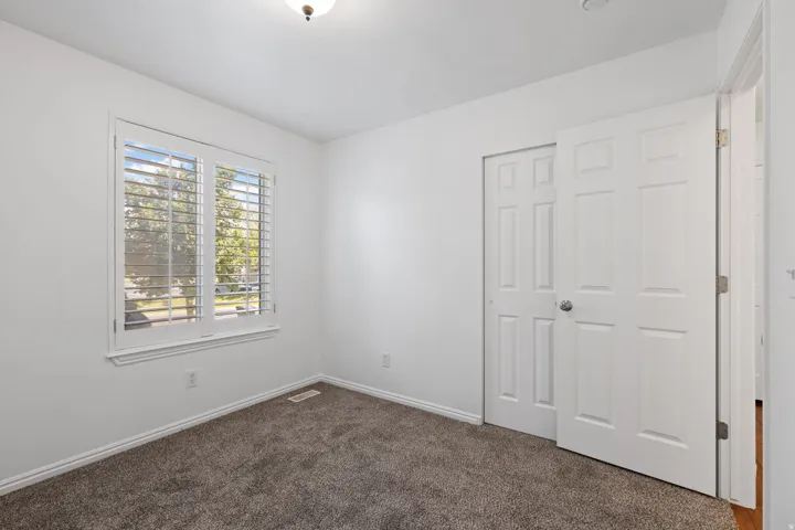 White walls, carpet flooring, window with plantation shutters, white paneled doors, and a ceiling-mounted light fixture