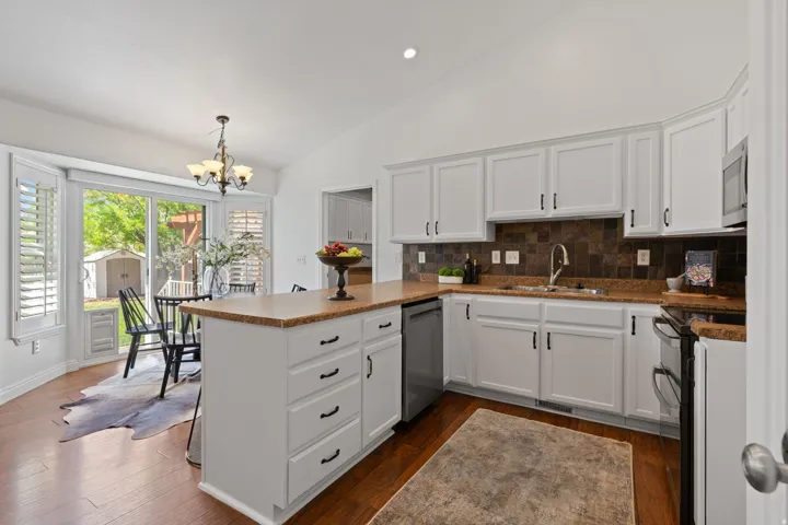Vaulted ceiling with recessed lighting, white cabinetry with dark hardware, stainless steel appliances, wood-finish flooring, and a sliding glass door