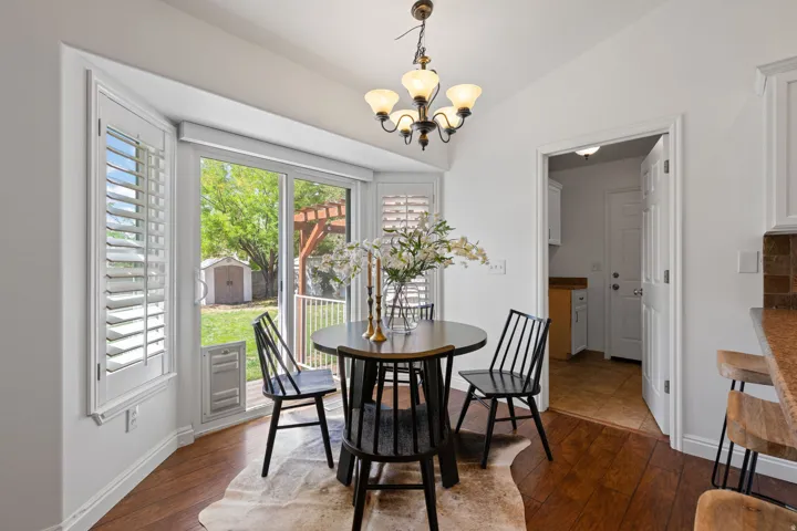 Wood-finish flooring with a bay window featuring plantation shutters, a sliding glass door, and a built-in storage shed
