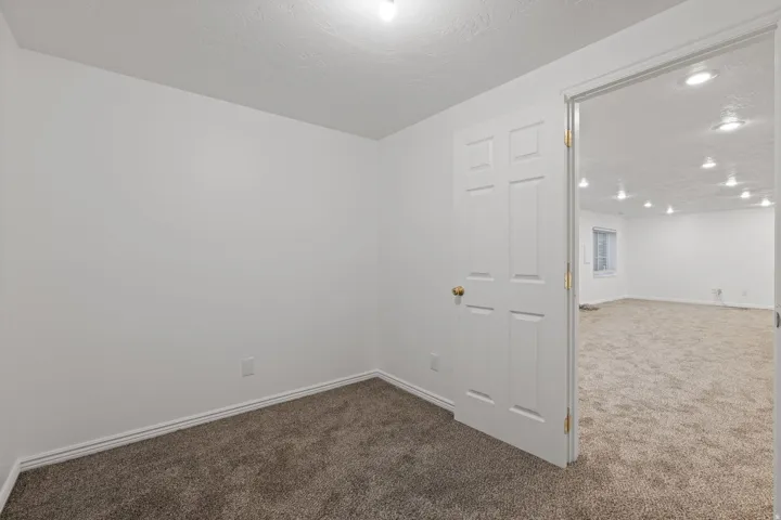 Carpeted flooring, white walls, white paneled door, gold door hardware, recessed lighting in background