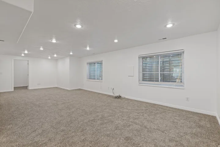 Expansive carpeted area with recessed lighting and two windows