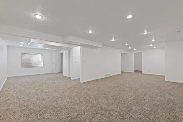 Expansive carpeted area with recessed lighting, white walls, and a window with horizontal blinds