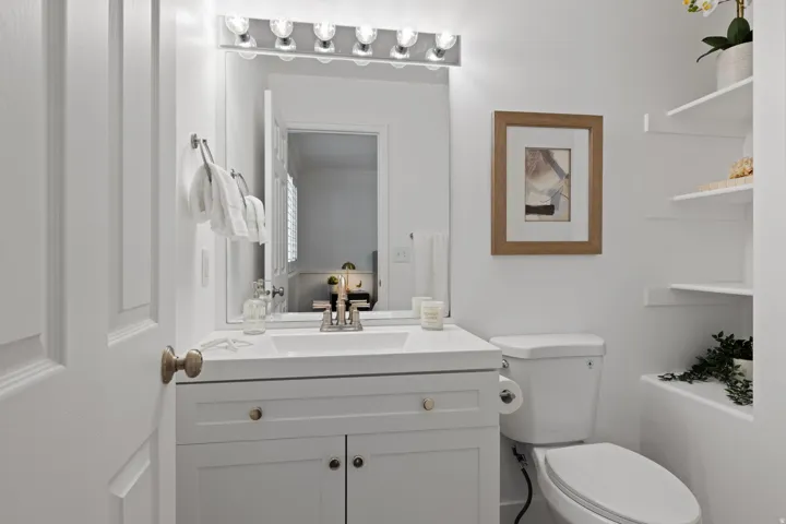 White vanity with a single basin sink, wall-mounted light fixture, and built-in shelving