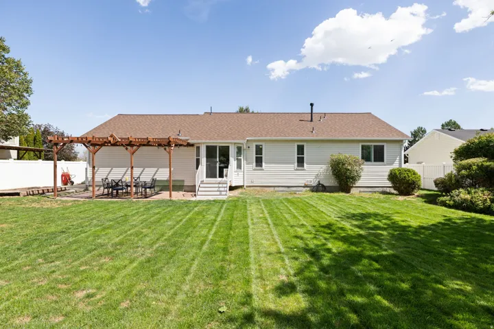 Expansive green lawn, wood pergola, paver patio, vinyl siding, and white fence