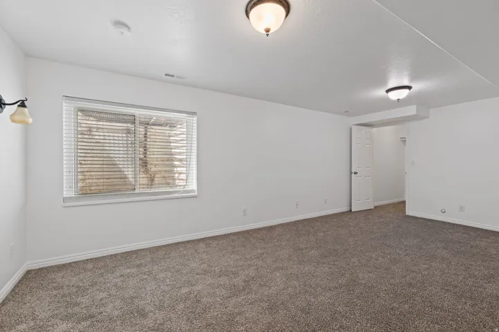 Spacious room featuring neutral carpeting, white walls, and a window with blinds