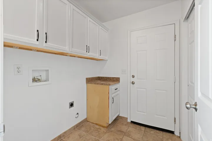 Utility kitchen featuring white cabinetry with brushed nickel hardware, wood-finish countertop, ceramic tile flooring, and direct access to the home's entry