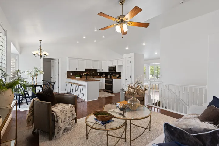 Vaulted ceilings with recessed lighting, wood-finish flooring, white kitchen cabinetry, kitchen island with breakfast bar, and plantation shutters