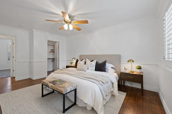 Rich wood-finish flooring, white beadboard wainscoting, crown molding, and a ceiling fan with integrated lighting