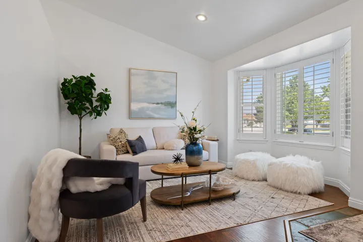 Bright living space featuring a bay window with plantation shutters, recessed lighting, and wood-finish flooring