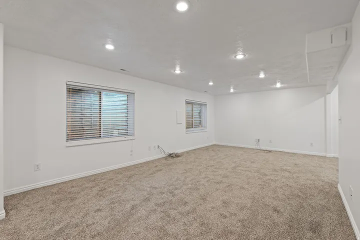Recessed lighting illuminating a spacious carpeted area with two windows featuring horizontal blinds