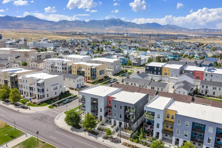 Modern residential community with diverse architectural styles, featuring multi-story buildings and townhomes, set against a backdrop of distant mountains