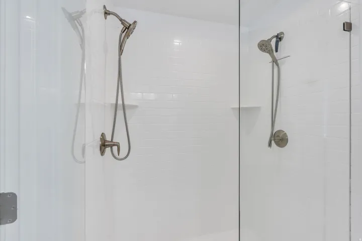 Shower enclosure featuring frameless glass, white subway tile, and a brushed nickel shower system with handheld spray