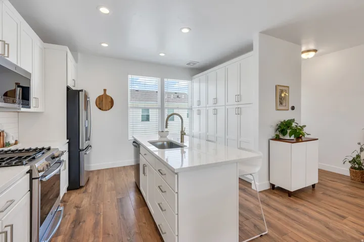 Recessed lighting, wood-finish flooring, white cabinetry, stainless steel appliances, and a central island with an integrated sink