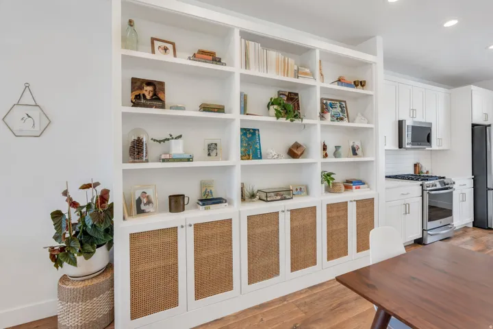 Built-in shelving with integrated closed storage, white cabinetry, stainless steel appliances, wood-finish flooring, and a subway tile backsplash
