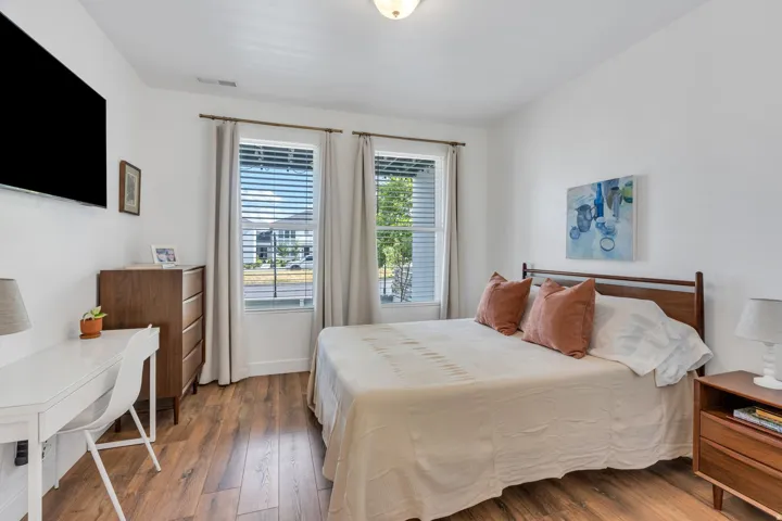 Wood-finish flooring throughout, bright white walls, two large windows with blinds, and a ceiling-mounted light fixture