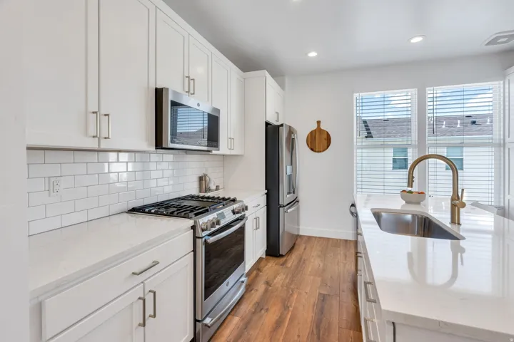 White shaker-style cabinetry, stainless steel appliances, white subway tile backsplash, solid surface countertops, and wood-finish flooring