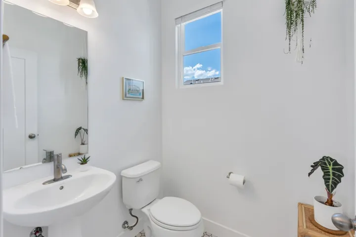 Pedestal sink, wall-mounted mirror, white toilet, single-pane window, and overhead vanity lighting