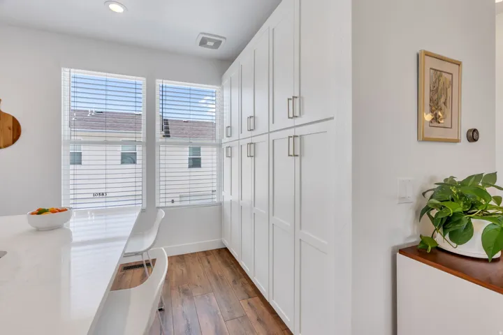 White shaker-style cabinetry with satin nickel hardware, wood-finish flooring, and a solid surface countertop