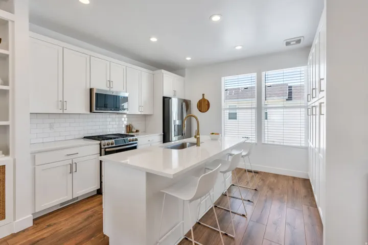 Kitchen featuring white cabinetry, subway tile backsplash, stainless steel appliances, a center island with seating, and wood-finish flooring