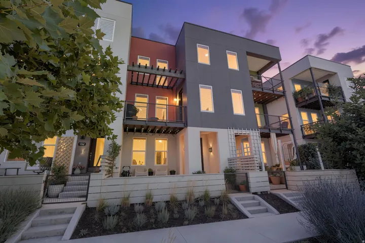 Modern multi-level facade with an integrated balcony, multiple windows, and a landscaped front yard with concrete steps