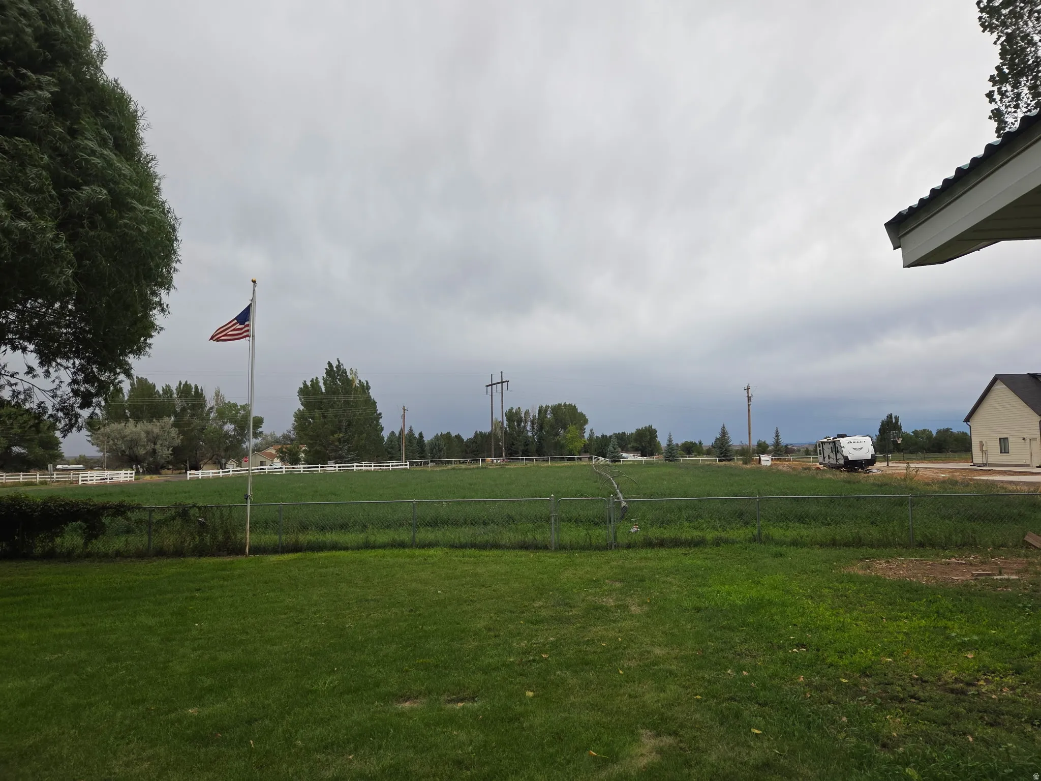 Expansive green lawn with a chain-link fence, a flagpole, and mature trees