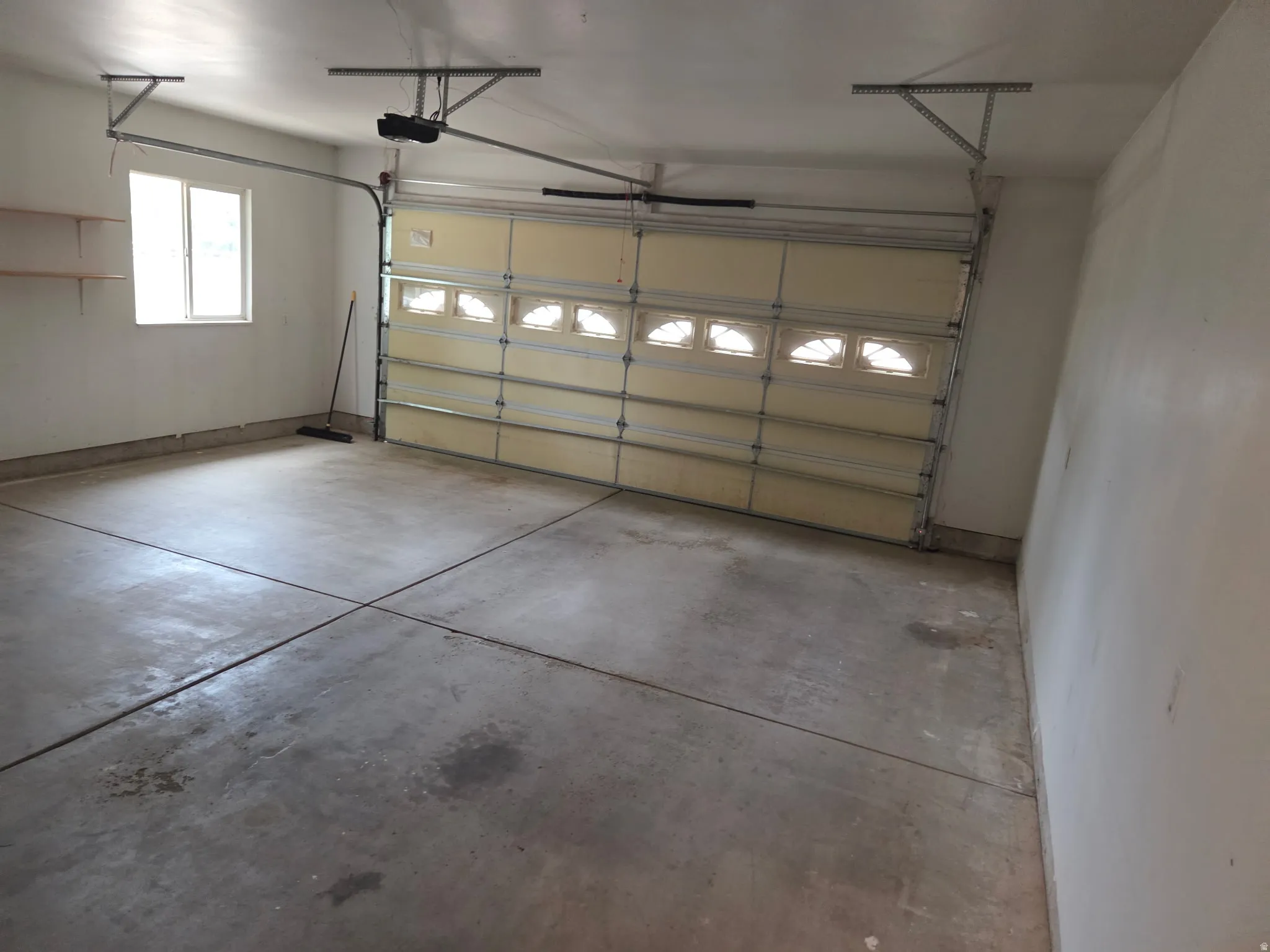 Attached garage with a sectional overhead door featuring window inserts, concrete flooring, and built-in shelving