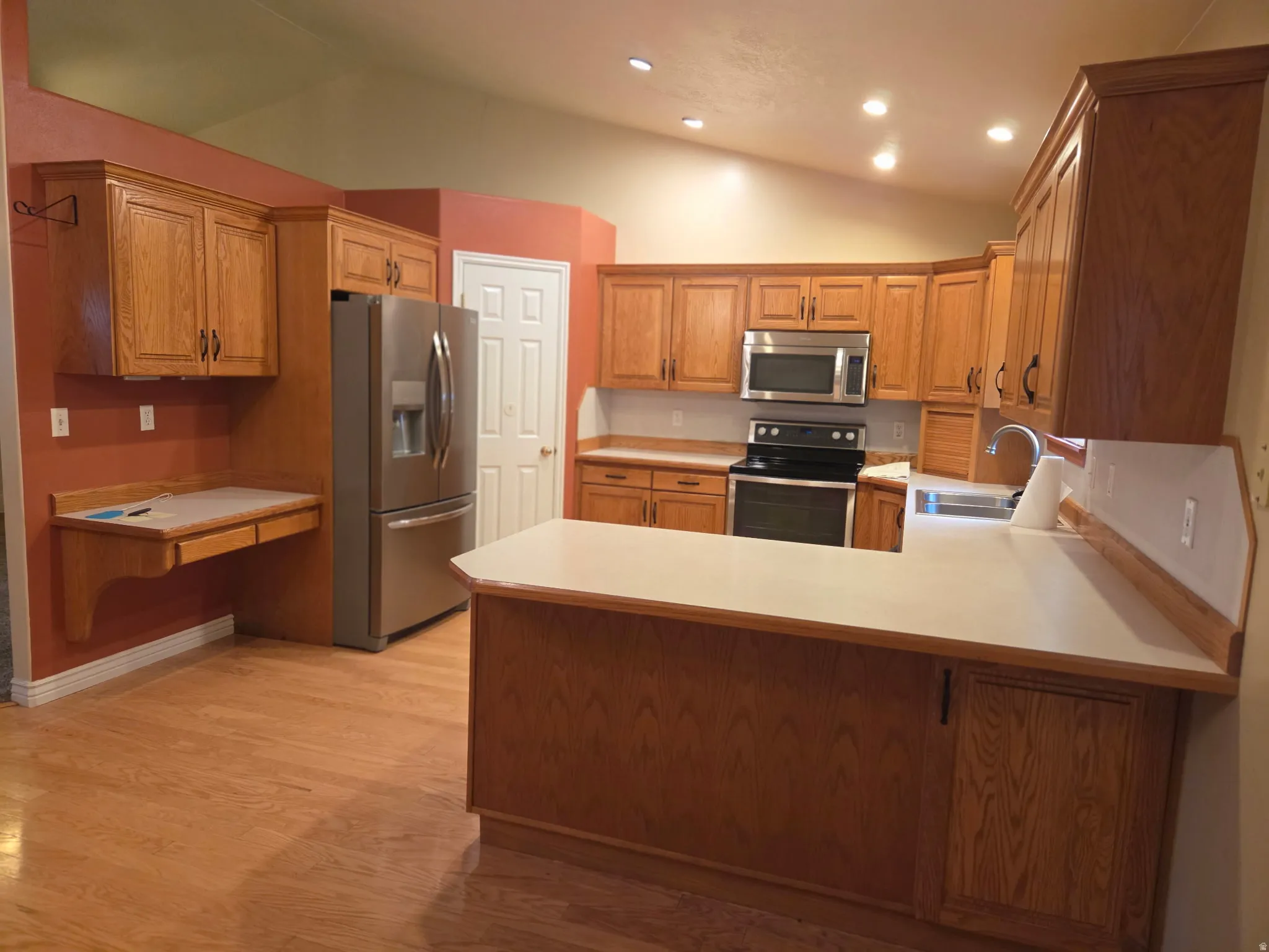 Kitchen featuring wood-finish cabinetry, stainless steel appliances, recessed lighting, wood-finish flooring, and a built-in desk area