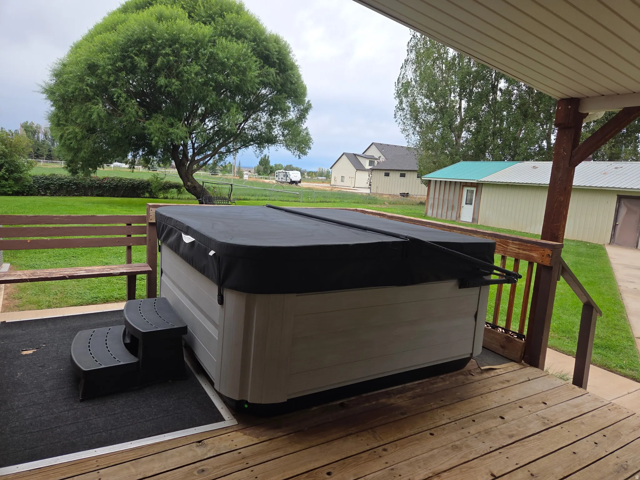 Wood deck with hot tub, exterior bench, and expansive green lawn