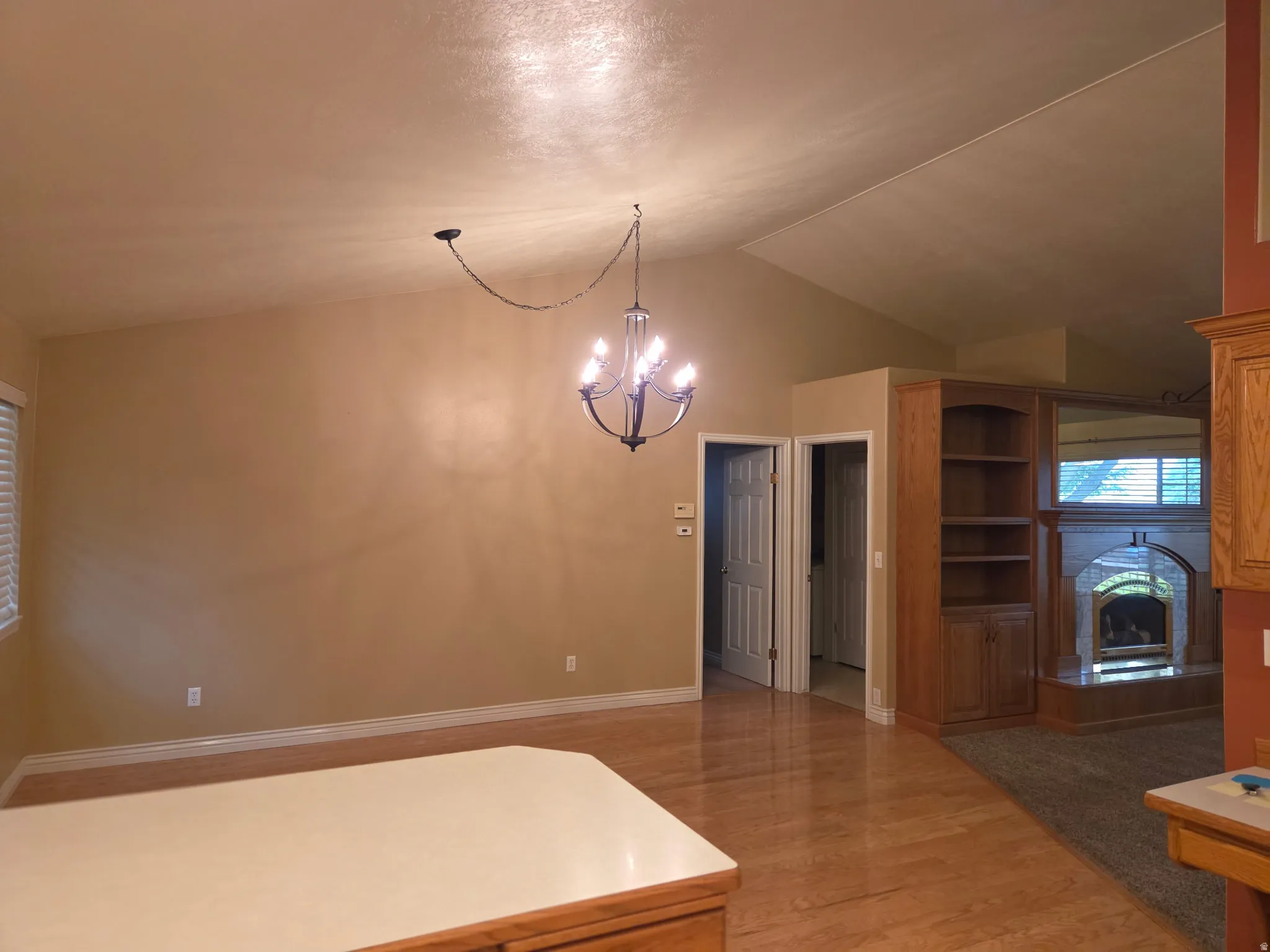 Vaulted ceiling with chandelier, wood-finish flooring, built-in shelving, and a fireplace with a hearth
