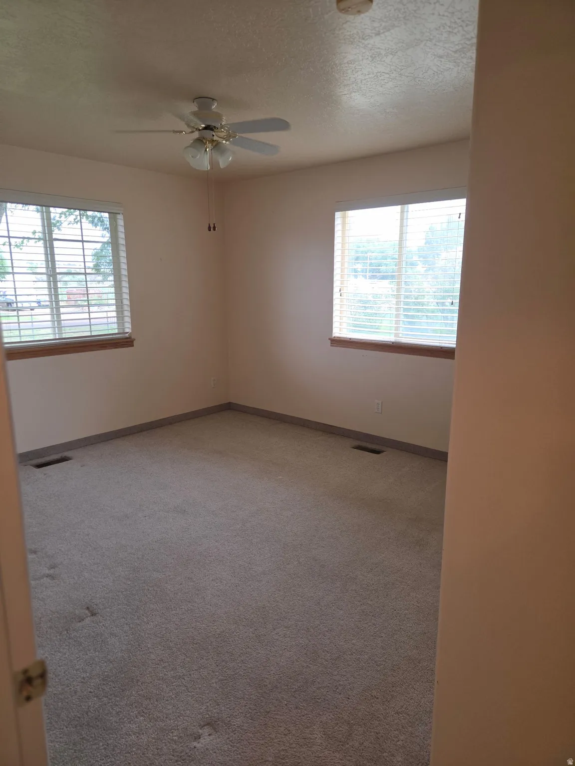 Wall-to-wall carpeting, two windows with blinds, and a ceiling fan with integrated lighting