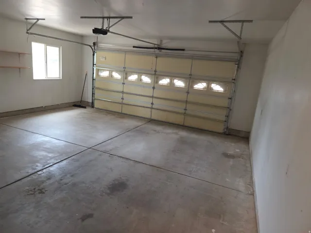 Attached garage with a sectional overhead door featuring window inserts, concrete flooring, and built-in shelving