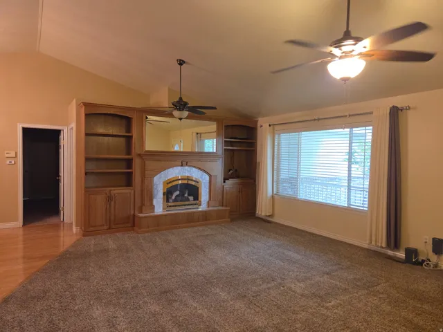 Vaulted ceilings with dual ceiling fans, a wide window with blinds, and a built-in media cabinet with a fireplace