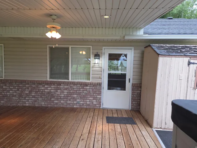 Expansive wood deck with a partial brick facade, overhead lighting, a ceiling fan, and an outdoor shed