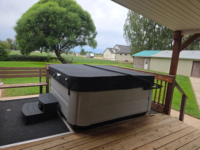 Wood deck with hot tub, exterior bench, and expansive green lawn