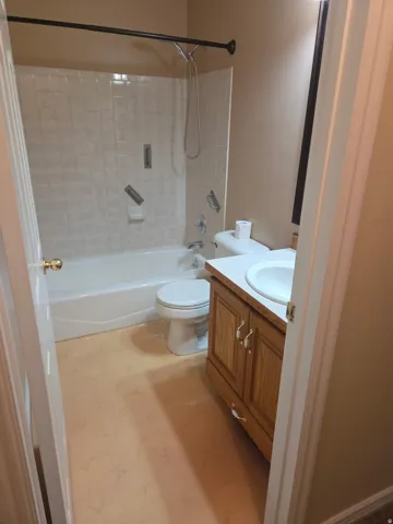 White tile shower surround, white bathtub, oak-finish vanity with white countertop, and single basin sink